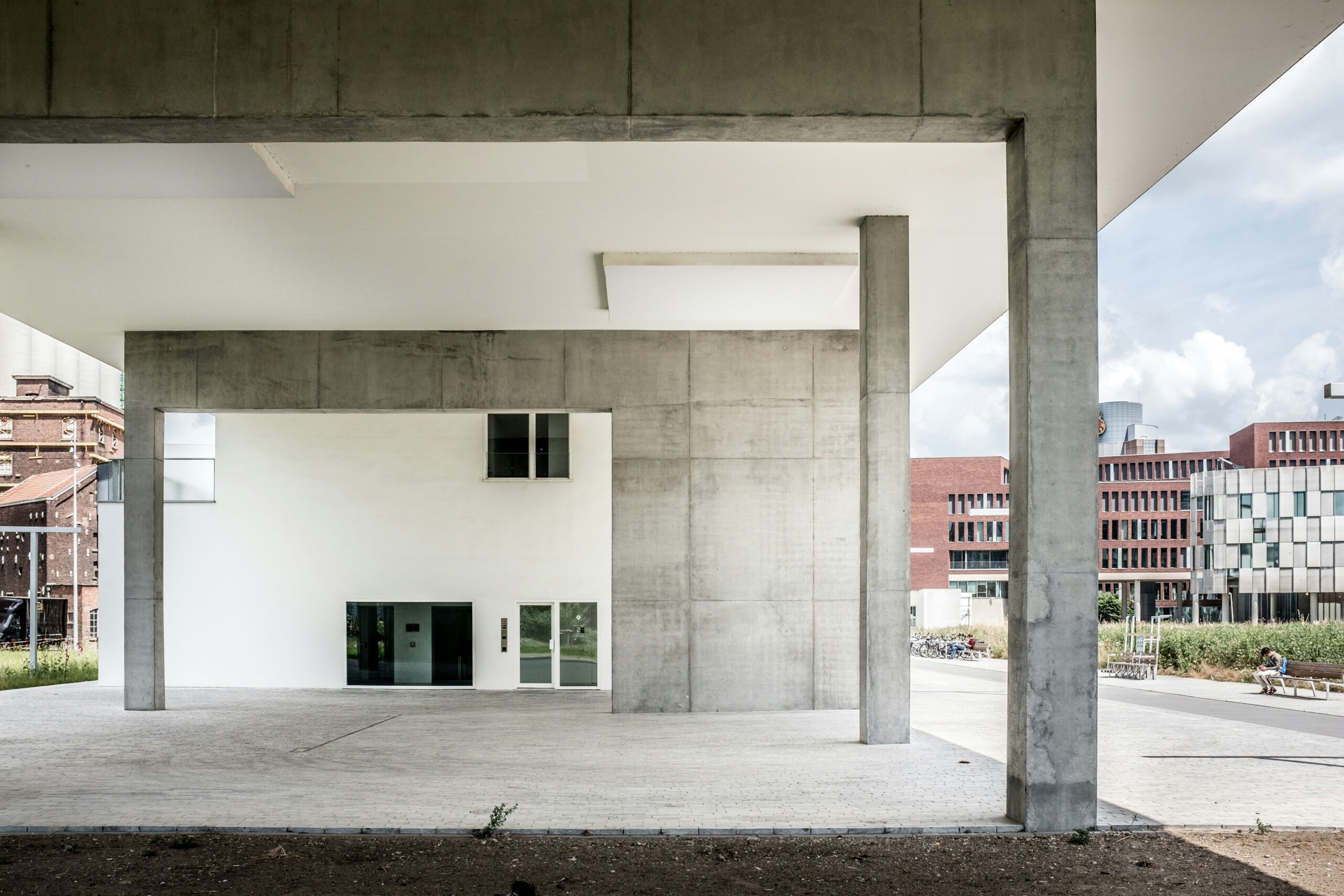 Modern architectural structure with large concrete columns and open space, showcasing minimalist design and urban development, representing continuous growth, with surrounding contemporary buildings and a clear sky in the background.